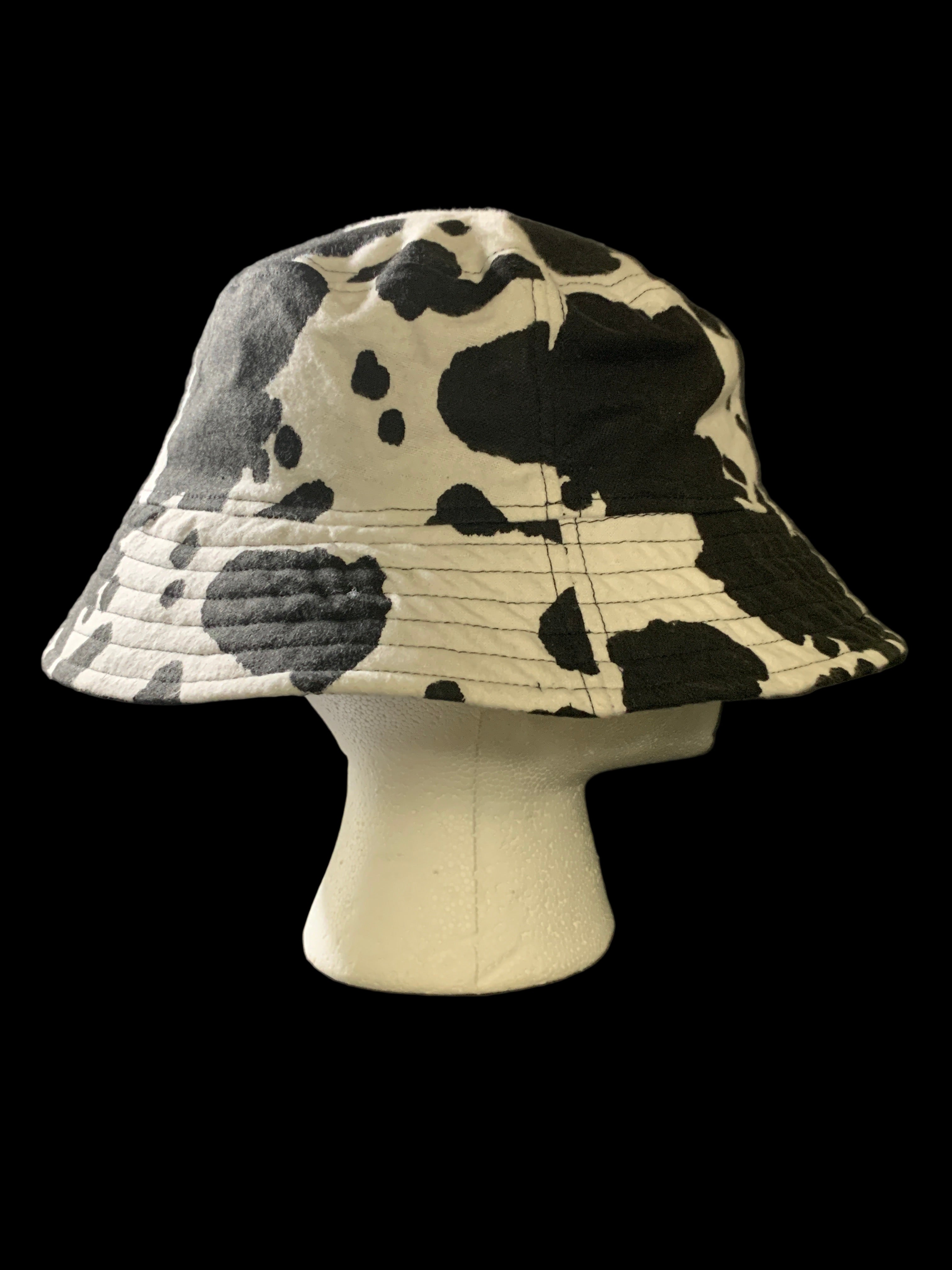 Cow print bucket hat on a mannequin head against a black background. Side view