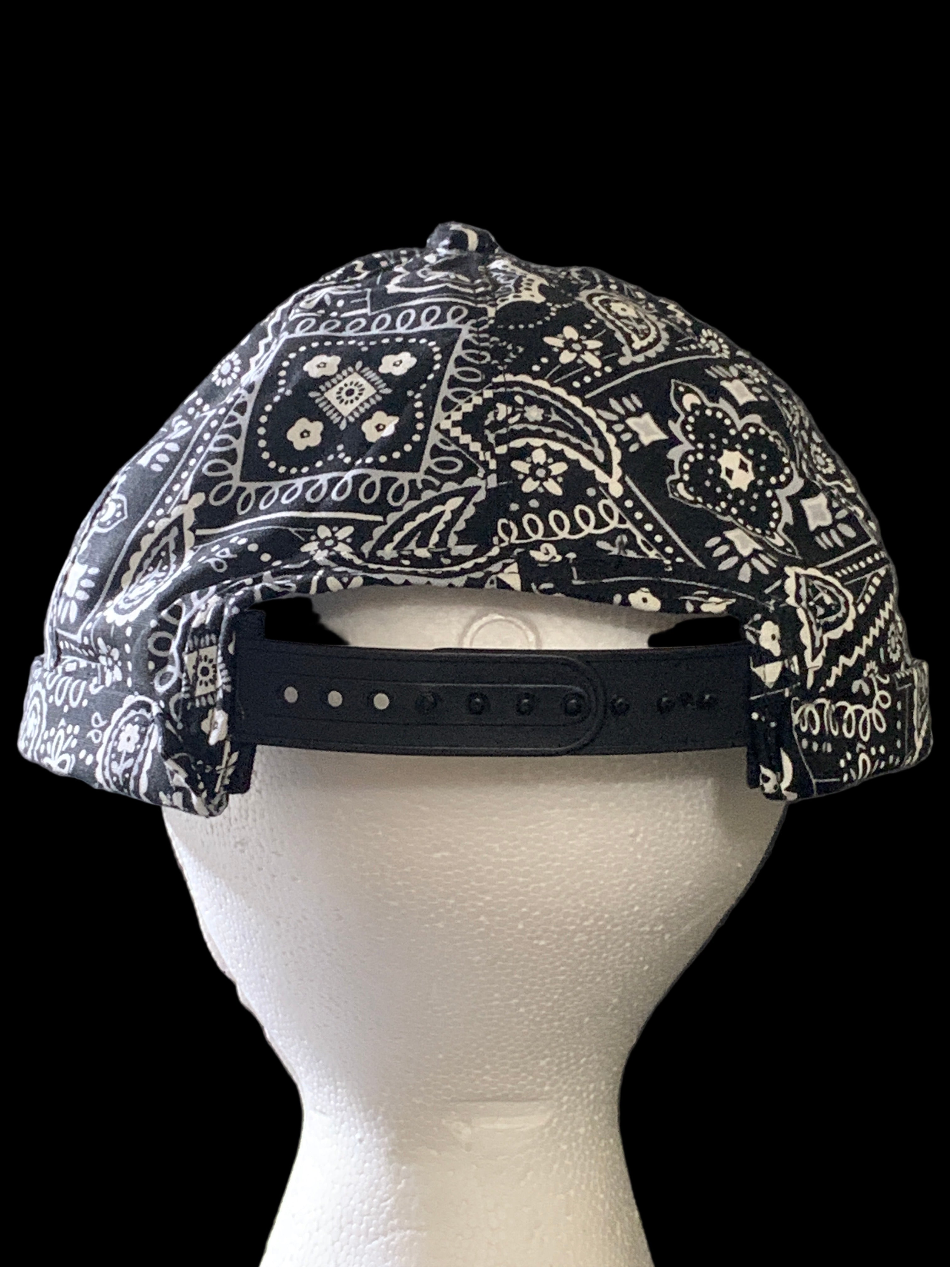Backside of  black paisley fabric roll cap hat with black snaps 