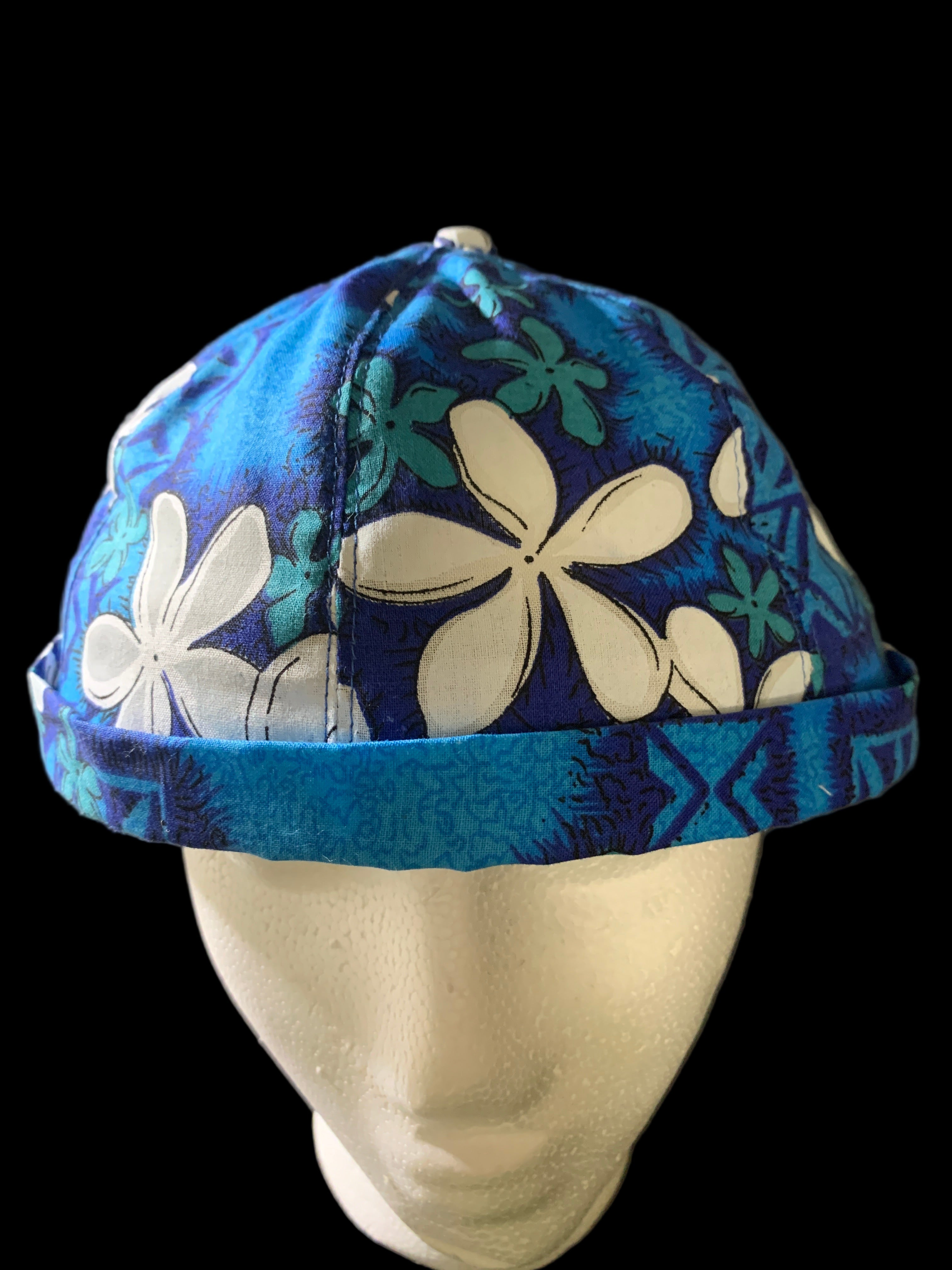 Polynesian Blue floral-patterned hat with button. Front view with black background. 