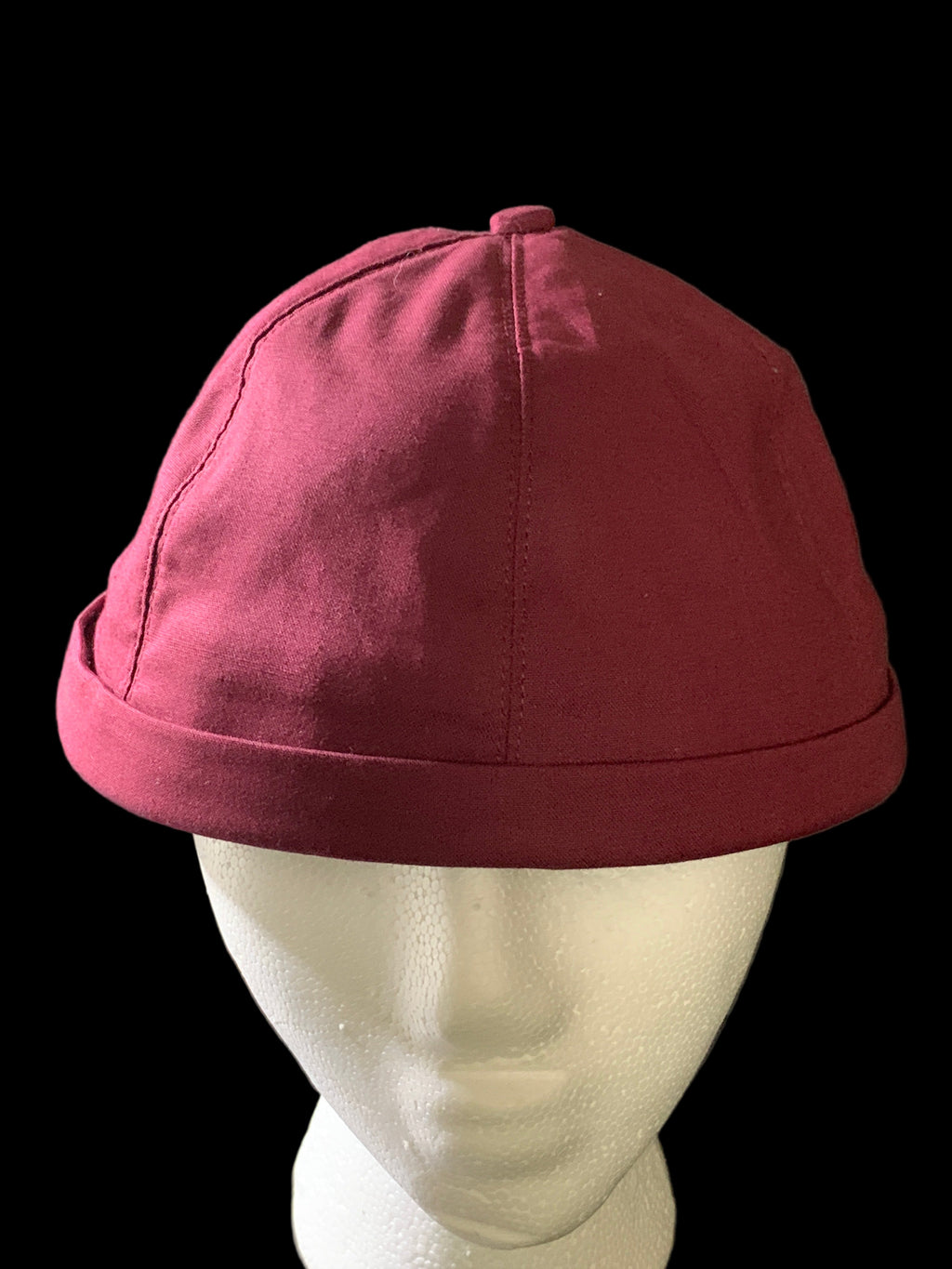 Front view of a burgundy roll cap hat with button and black background. 