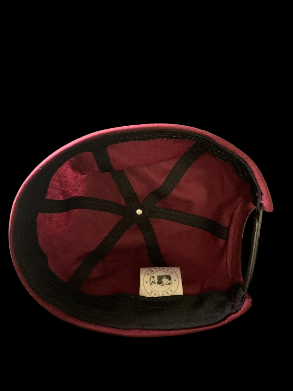 Inside view of a burgundy hat with white tag and black trimmings. 