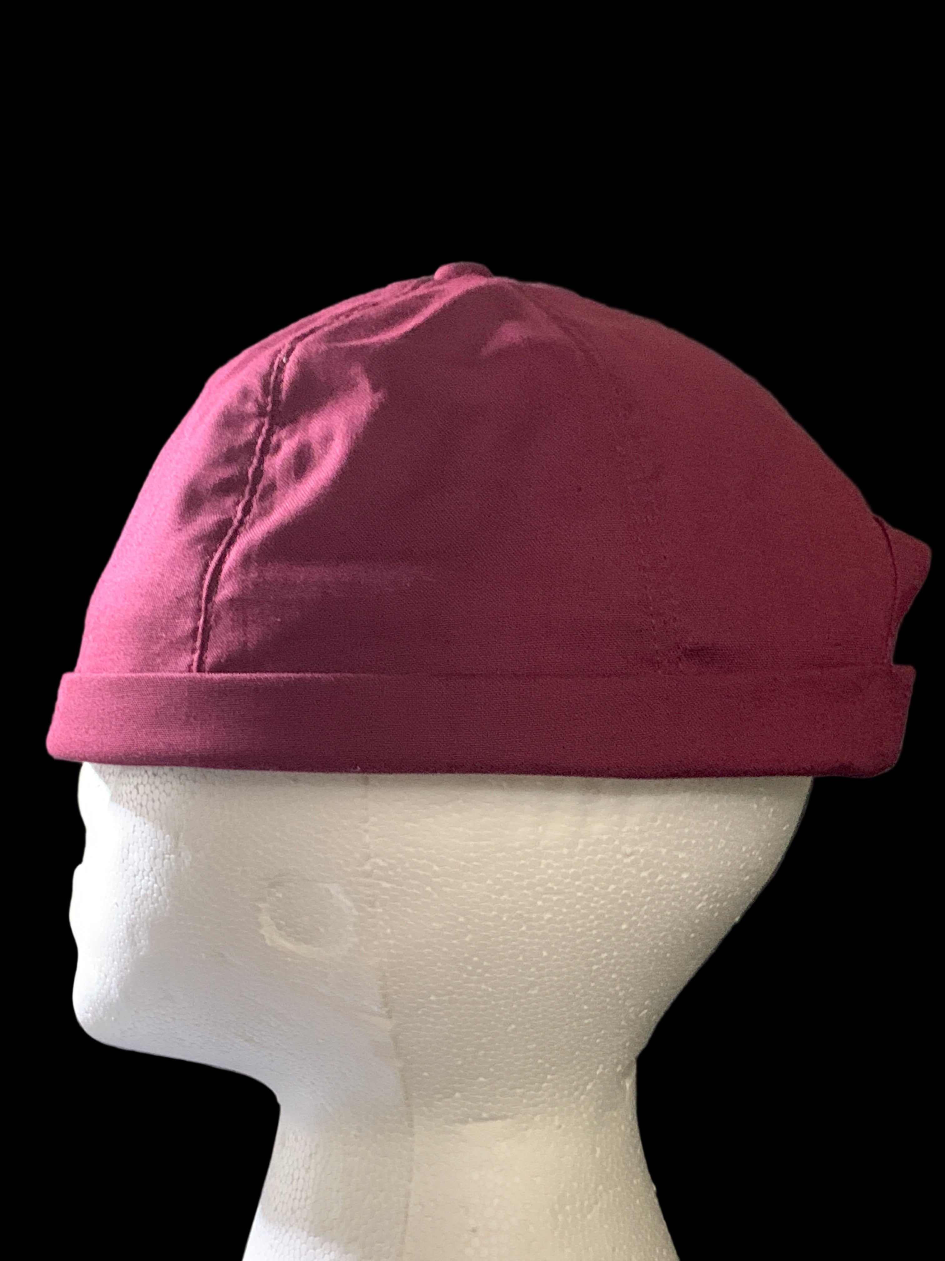 Side view of a Burgundy roll cap hat with botton  and black background. 