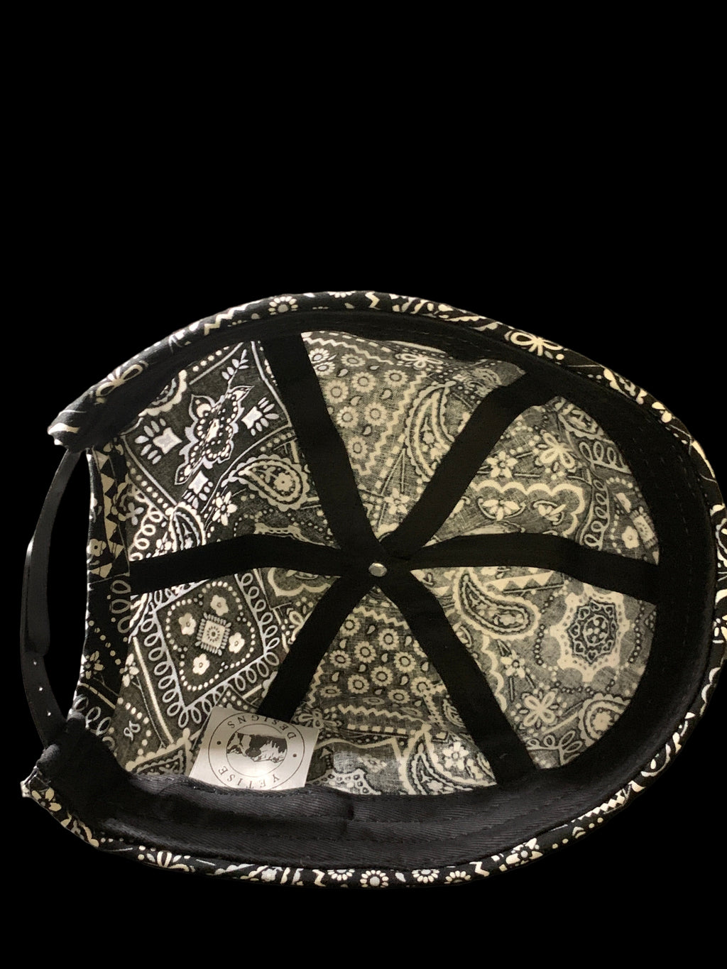 Inside of a black paisley roll cap hat with white tag and black trimmings. 