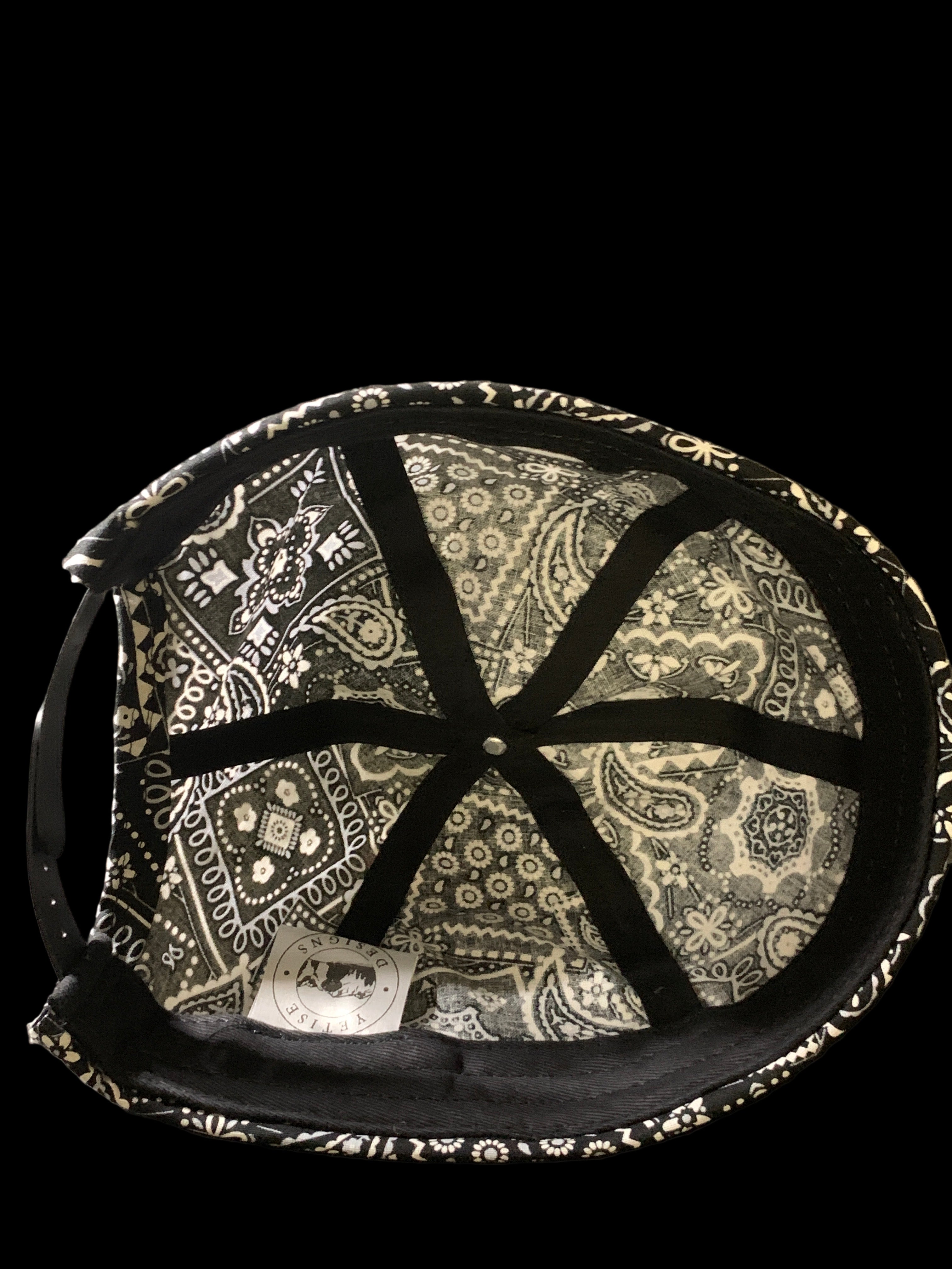Inside of a black paisley roll cap hat with white tag and black trimmings. 