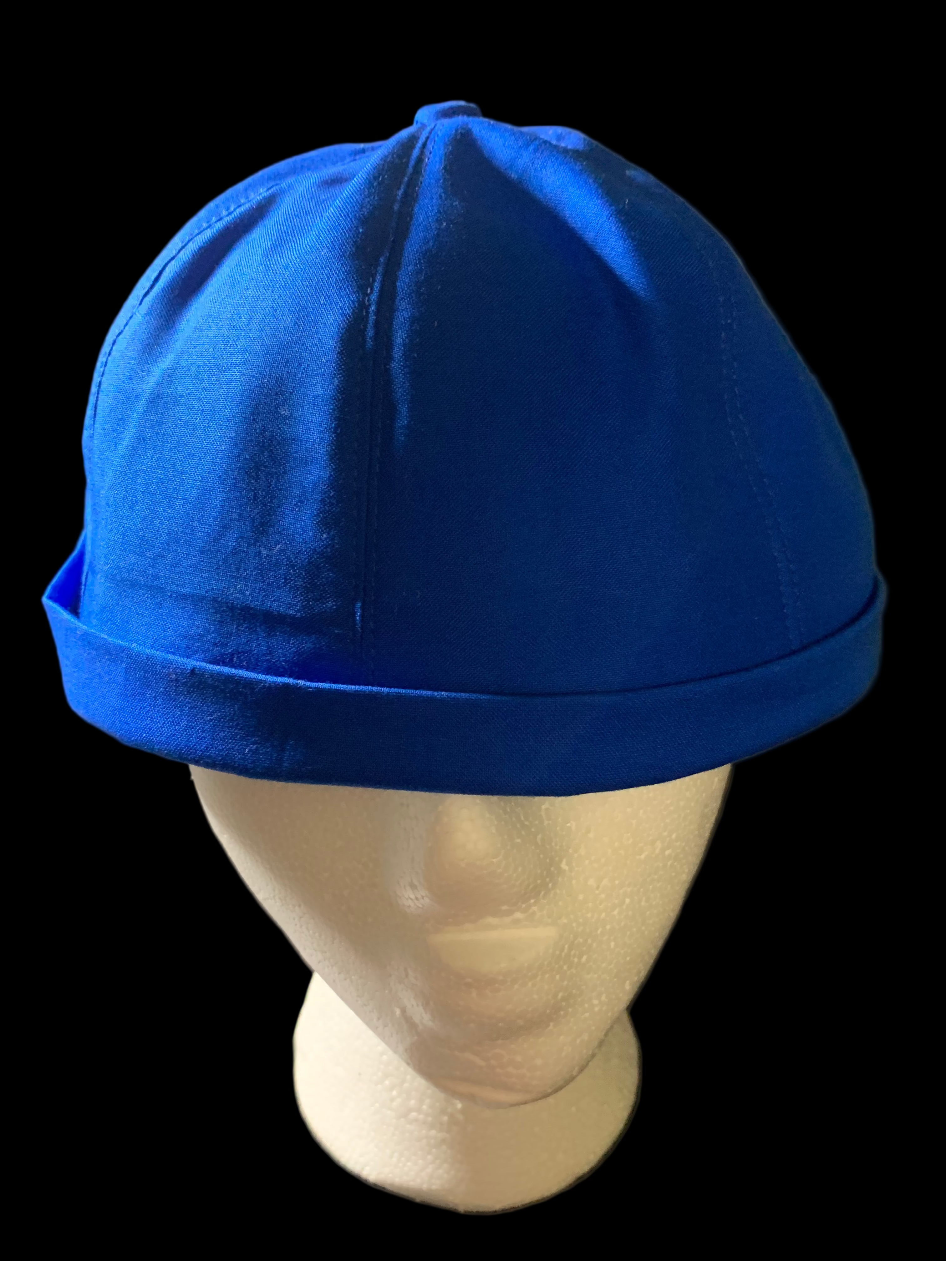 Front view of  blue hat with blue button and black background. 